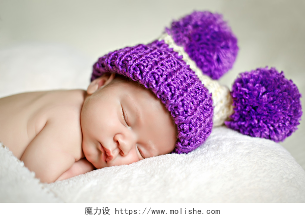 正拍一名带着紫色帽子的婴儿睡在白色床上可爱新生婴儿睡在一顶帽子